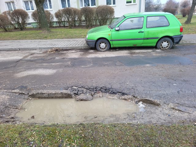 Ciężarówki rozjeżdżają trawnik, wrak blokuje chodnik i ulicę. Nikt nie poczuwa się do tego, aby go uprzątnąć (zdjęcia)