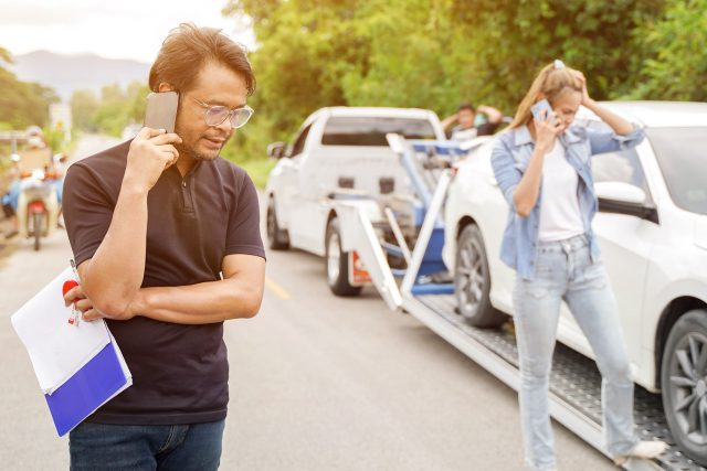uczestnicy kolizji rozmawiają przez telefon stojąc na tle samochodu gotowego do transportu na lawecie