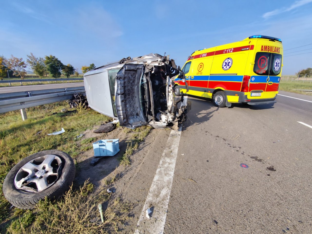Przewrócony pojazd i karetka przy drodze